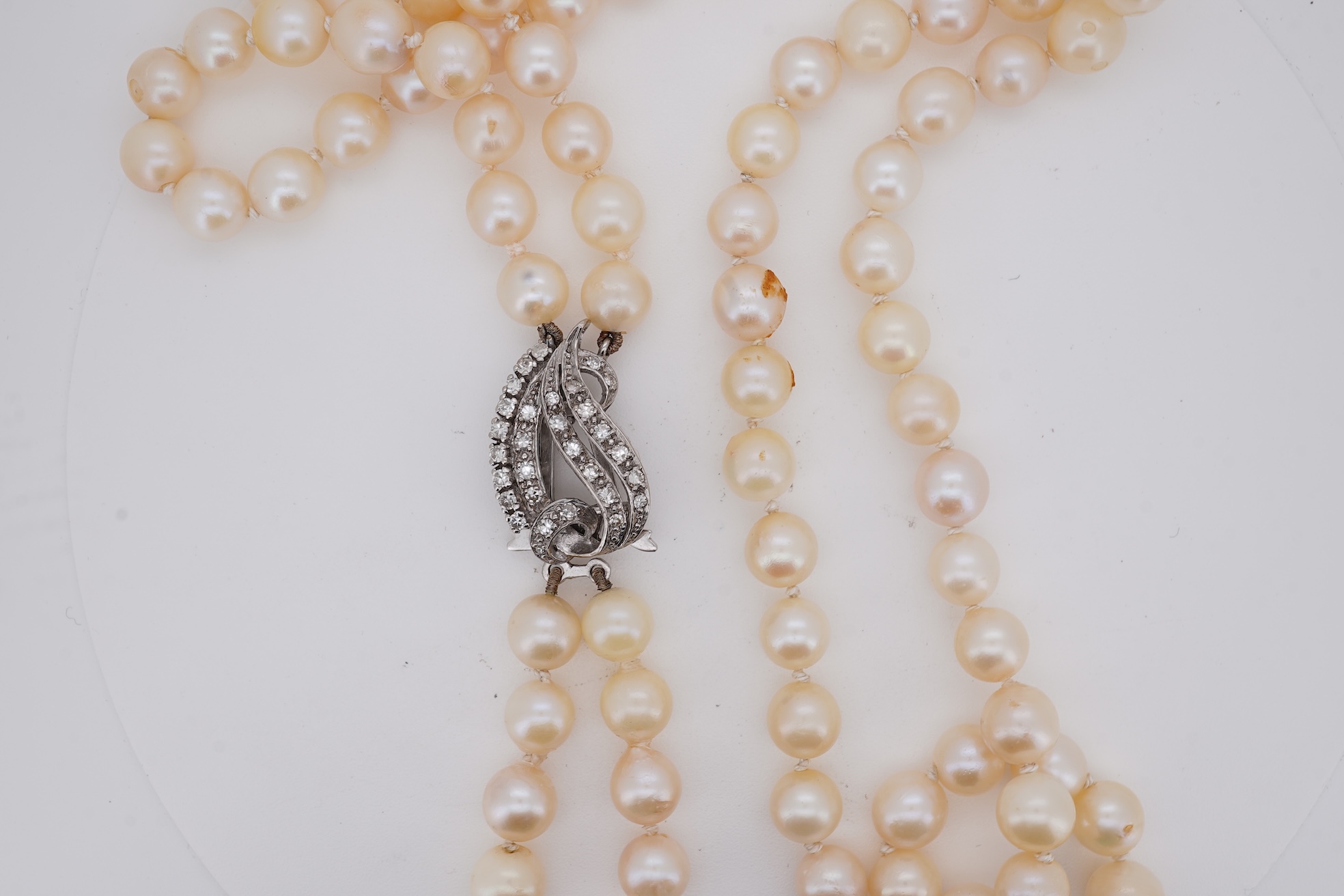 A twin strand cultured pearl necklace with a diamond cluster set white metal scroll shaped clasp, 60cm.